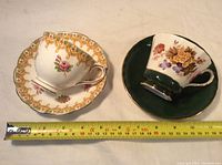 Two royal Albert and Ansley china teacups each with matching saucers, placed beside a measuring tape showing size.