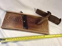 Wooden cabbage mandolin with metal blade and attached handle lying next to a measuring tape showing about 14 inches in length; metal wedge and RR spike beside it.