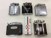 Six vintage pocket lighters in varying designs and finishes, displayed on white surface.