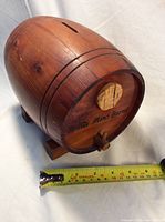 Front angled view of the wooden keg coin piggy bank with measuring tape showing length.