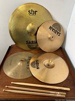 Overall view of four cymbals and three drumsticks arranged on wooden surface