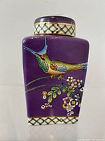 Front view of the antique tapered porcelain tea caddy with a purple background and hand-painted kingfisher bird motif and floral decoration.