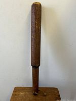 Full view of wooden police truncheon standing upright against wall, showing full length and shape.