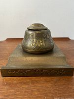 Front view of the bronze inkwell placed on the stand, showing embossed Art Nouveau motifs.