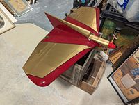 Top angled view showing large delta wing shape with metallic gold and red paint, twin propellers on front, and streamlined fuselage.