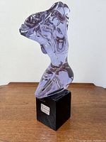 Front view of full purple glass torso sculpture on black base on wooden surface.
