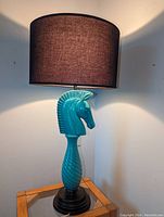 Front and side view of the turquoise rook-shaped table lamp illuminated to show details.