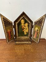 Front view of vintage Florentine triptych wooden panel icon with open wings showing angels on side panels and central Madonna and child.