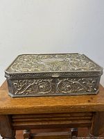 Front view of the rectangular silver plated jewelry box showing embossed floral patterns and patina.
