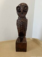 Front view of the carved wooden owl statue with detailed facial features, perched on a rectangular base.