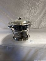Front view of the polished stainless steel chafing dish on white cloth background, showing the base and handles.