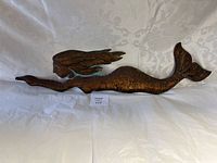 Full view of the copper mermaid horizontal wall sign on a light fabric background, showing the entire figure lying horizontally.