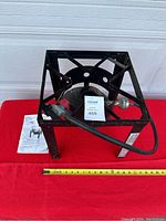 Black metal propane burner stand with hose and regulator on red background and measuring tape