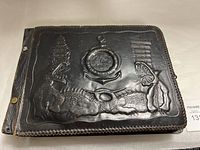 Front cover of black leather album embossed with crocodile/alligator motifs and central anchor emblem