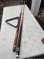 Two pool cues laid out on a white table with a triangle rack and chalk cube visible, showing overall look and size.