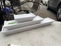 Set of three white rectangular wall shelves stacked, showing front and top surfaces.