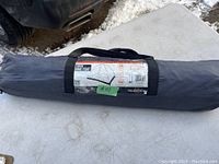 2 Man dome tent packed in gray carry bag laid on white table outdoors with part of a black vehicle visible nearby.