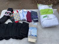 Photo showing a mixture of black ribbed knit socks, novelty patterned colorful socks, one pair of thick white knit socks labeled 'Extreme Extreme' Size Small, and a bundle of packaged white sports socks (7 pairs).