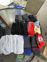 Several pairs of socks spread on glass table, mostly black, white and some colorful festive patterns.