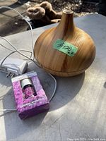 Photo of wood grain aroma diffuser with power adapter and lavender essential oil bottle in purple box placed on outdoor surface.
