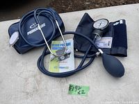 Blood pressure monitor set including inflation bulb, pressure gauge, arm cuff, stethoscope, carrying case, and manual on table.