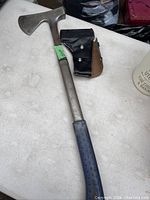 Full view of the vintage Eastwing axe laid on a white surface showing the metal handle, axe head, and sheath next to it.
