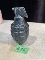 Front angled view of the black cast iron WWII pineapple grenade replica, showing the segmented body and metal lever on top.