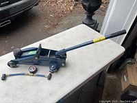 Photo of hydraulic trolley jack with handle, pressure gauge hose on white table