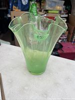 Front angled view of large green art glass vase showing wavy ruffled rim and green translucent glass.