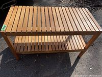 Photo of a rectangular solid wood console/side table with slatted wooden top and lower shelf, viewed from above under natural daylight.
