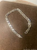 Single sterling silver chain bracelet laid flat on brown surface showing geometric interlocking chain links with lobster clasp.