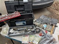 Overall view of open black tool box with tools inside on a table, showing hammer, wrench pouch, electrical tape, and various hand tools alongside box