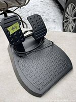 Photo showing a black pedal set with brake and gas pedals and attached cable on a textured surface with some snow in the background.