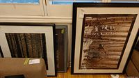 Three framed nature prints leaning against a wall: dark framed print with birch trees and a moose, forest path print, and another forest scene.