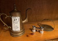 Brass coffee pot, Birks opera glasses with mother of pearl style inlays, and brass napkin holder displayed on wooden shelf.