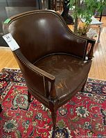 Side angle view of the brown leather upholstered wood frame arm chair showing tack detail and wear on seat and armrest.