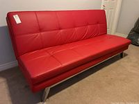 Front view of red faux leather convertible sofa bed with tufted seat and back