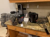 Kitchen countertop showing various kitchen appliances: Sodastream soda maker, small black blender, white Cuisinart food processor, Universal food/meat chopper, black electric kettle, black hot plate warmer with cord.