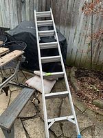 Metal ladder in folded and extended positions outdoors against a wooden fence and patio furniture, showing overall condition and structure.