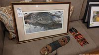 Photo showing the framed Seerey-Lester print featuring raccoons and two carved wood masks placed on a sofa.