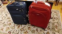 Photo of two Samsonite soft side suitcases, navy blue and red, placed on a patterned carpet with additional furniture in the background.