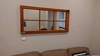 Full view of the mirror hanging on the wall above a sofa, showing the reflective window pane style with six sections and pine wood frame.