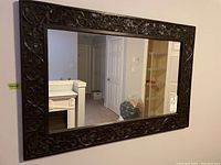 Full view of the rectangular wall mirror hung on a wall, showing the carved wooden frame and reflective glass.