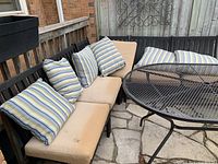 Six connected metal framed outdoor chairs forming two benches with beige and striped cushions and a round black metal mesh patio table.