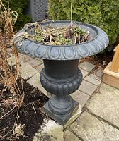 Front angled view of the cast iron planter showing the decorative rim, fluted body, soil and dried plant inside, and some rust on finish.
