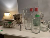 Wide view of lot with ceramic pots and various clear glass vases and candleholders, lamp and furniture partially in background