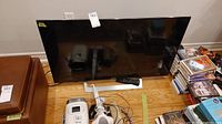 Full front view of Sony TV and remote placed on floor beside other items.