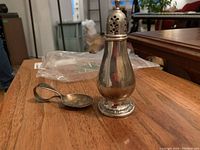 Salt shaker and child's spoon placed on wood surface showing their size and condition.