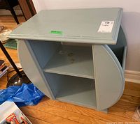 Photo showing front angle of wood side table painted light blue, with two center shelves and curved magazine racks on sides, some finish flaws visible.