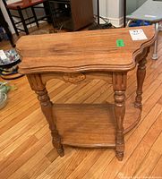 Front view of the wood side table showing detailed turned legs, beveled tabletop edges, lower shelf, and floral carved medallion on apron.